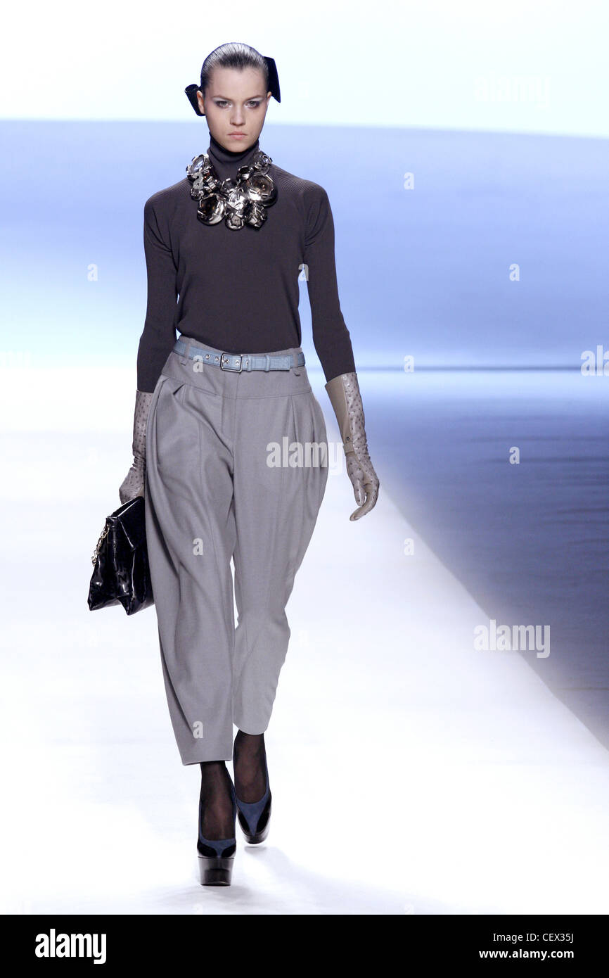 Model wearing grey pleat front cropped trousers, poloneck top, leather gloves, chunky necklace, high wedge sole shoes Stock Photo