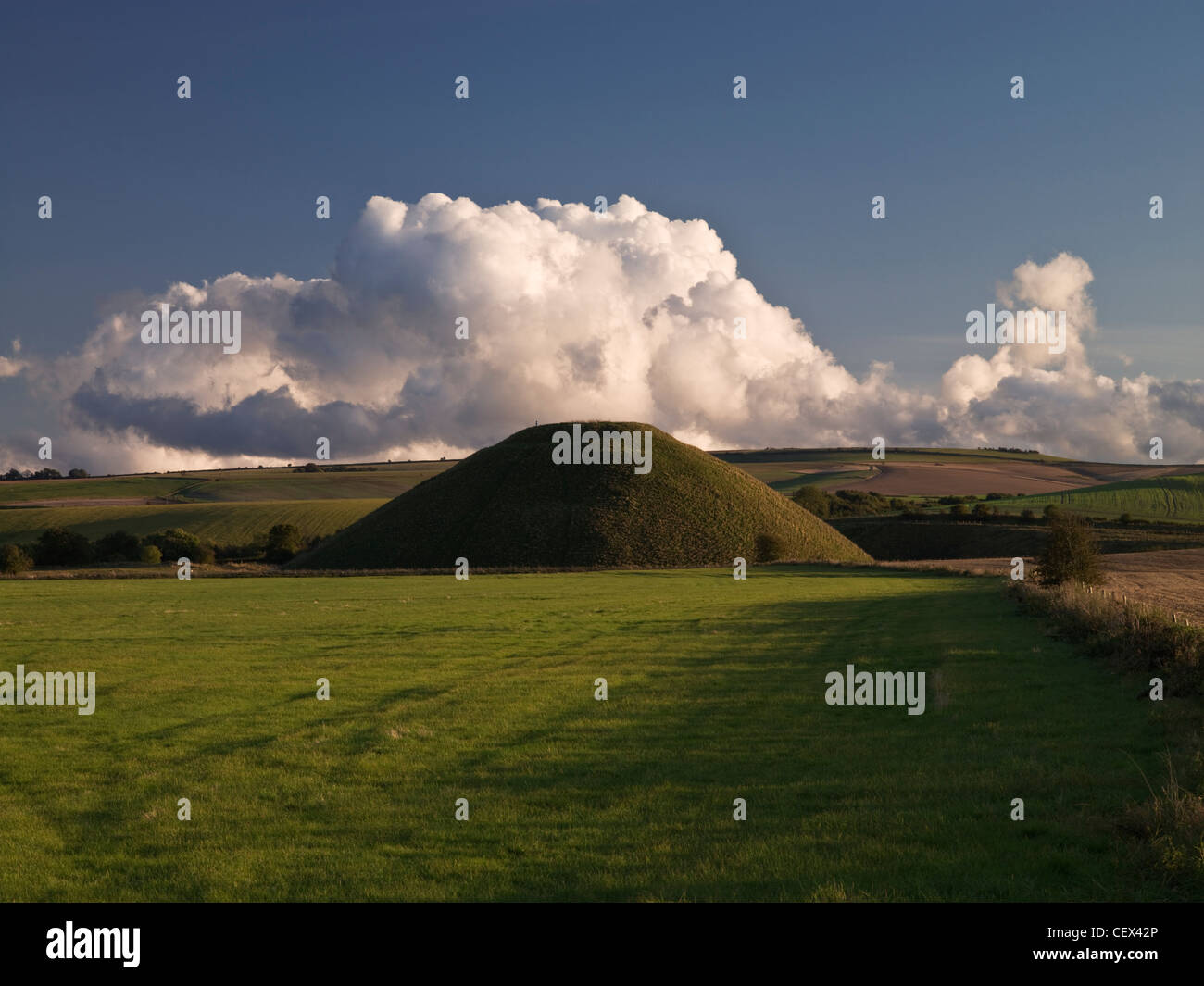 View of Silbury Hill, the tallest prehistoric human-made mound in Europe, against a bank of cloud on a clear evening. Stock Photo