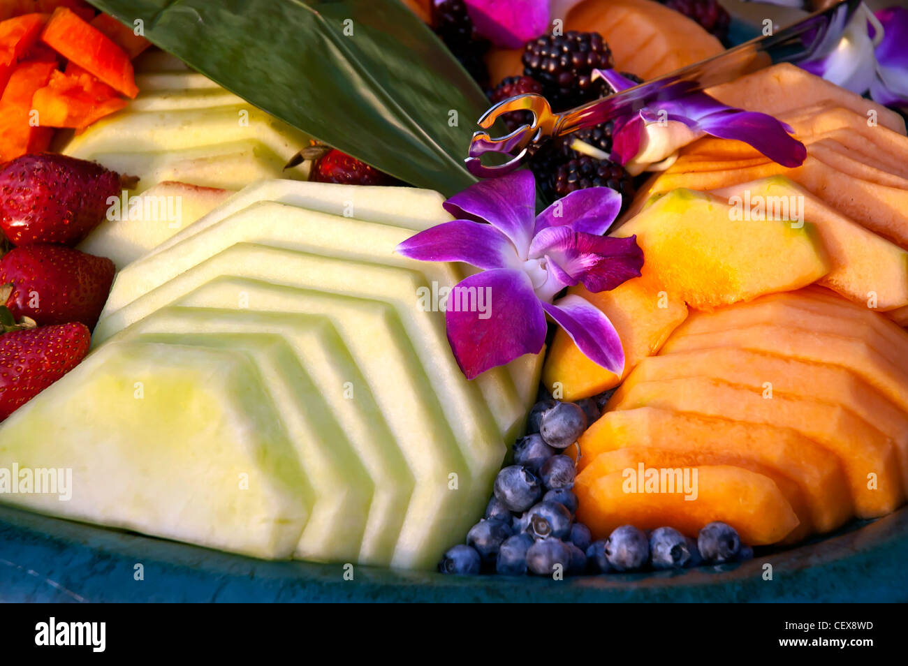 Tray of different seasonal and tropical fruit bright colors decorated with purple orchid blossoms Stock Photo