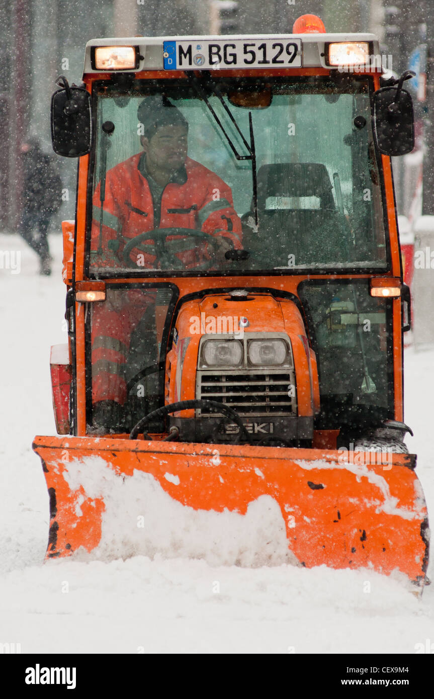A snow plow with driver hard at work clearing the streets of Munich