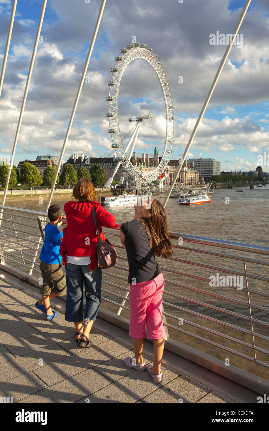 A mother and her children enjoy the view of the London Eye from the Hungerford Bridge over the river Thames Stock Photo