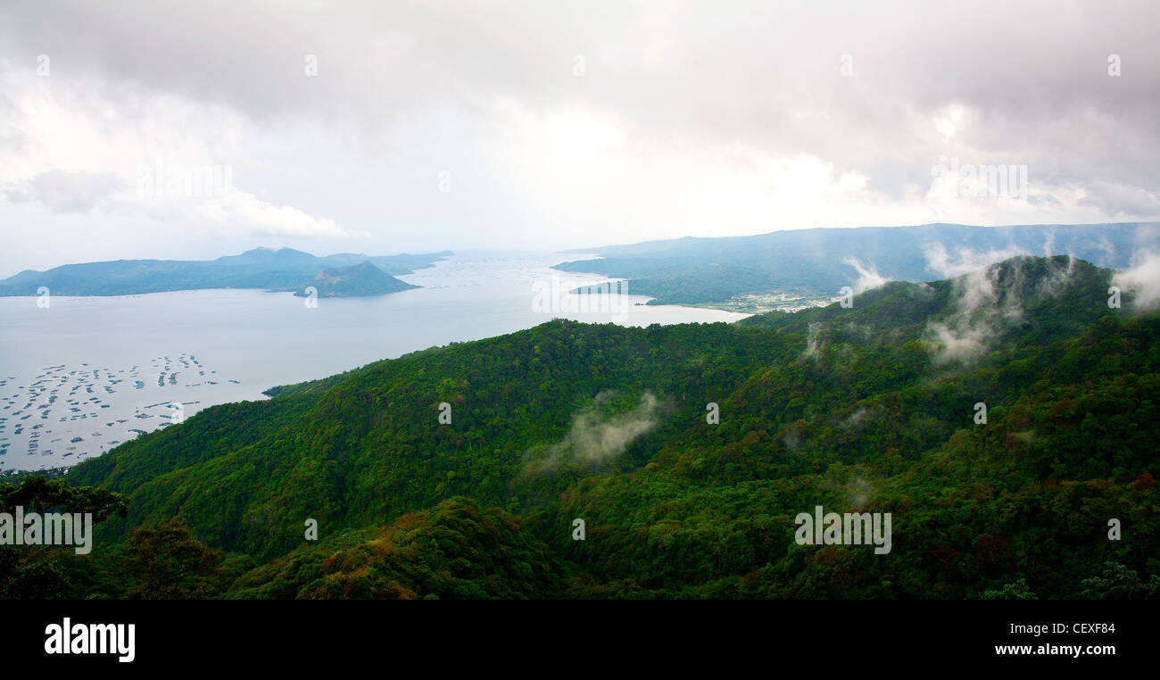 Morning fog rises off of the rain forest covering the slopes of Tagaytay as Volcano Island and Taal Lake sits in the background. Stock Photo