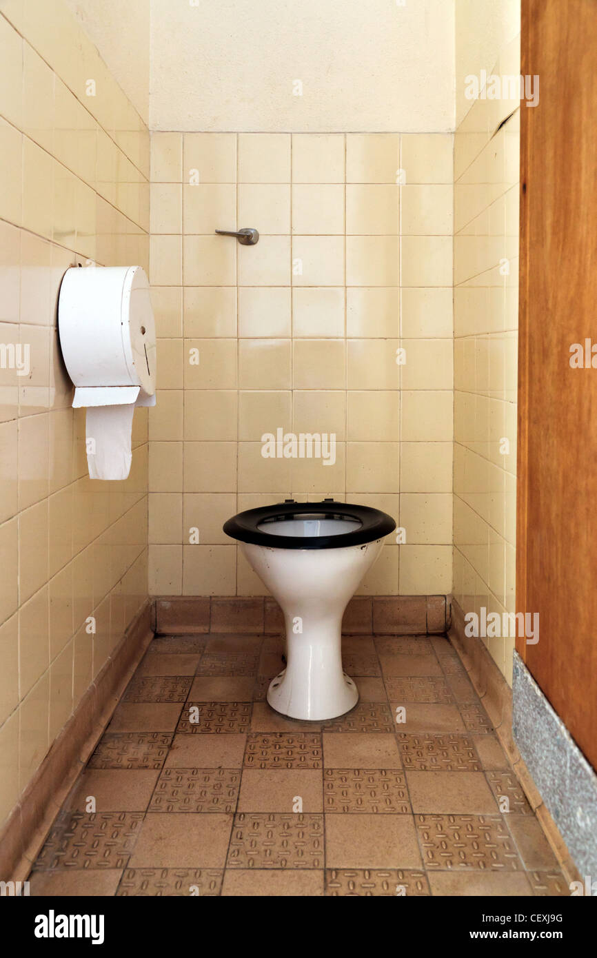 Photo of a public toilet with part of the seat missing, the floor, walls and bowl are stained and dirty. Stock Photo
