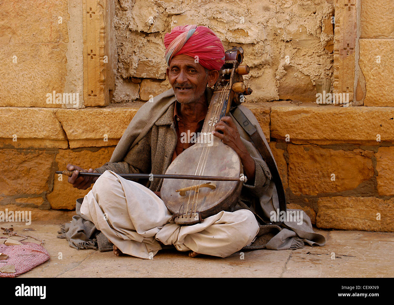 Senior Rajput man busking joyful recited music playing on hand made violin 'veena' entertaining public in street for donations. Stock Photo