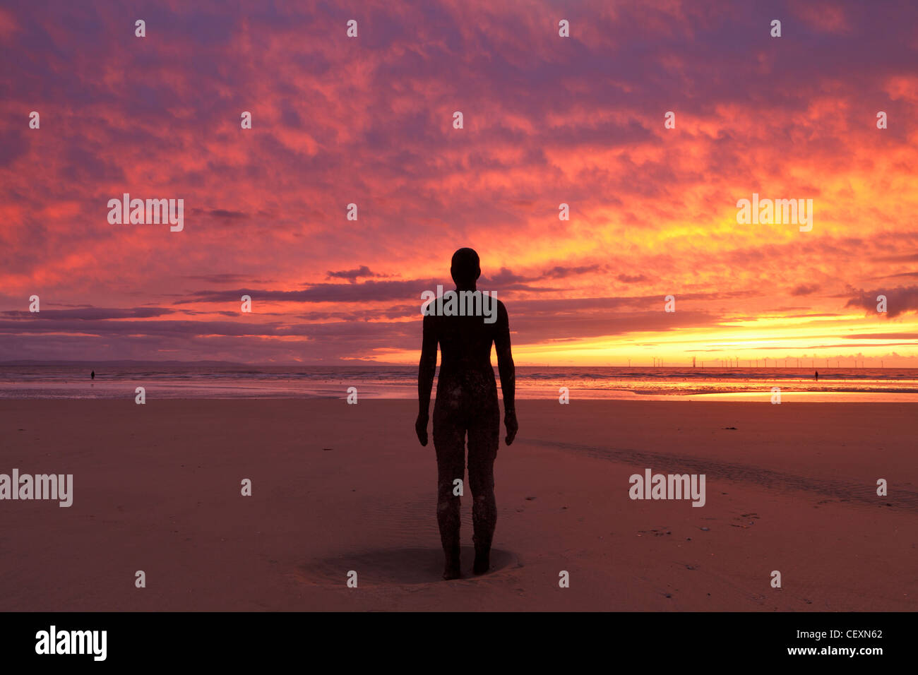 Firey Sunset over Crosby Beach, with one Antony Gormley's Statues Silhouetted. Stock Photo