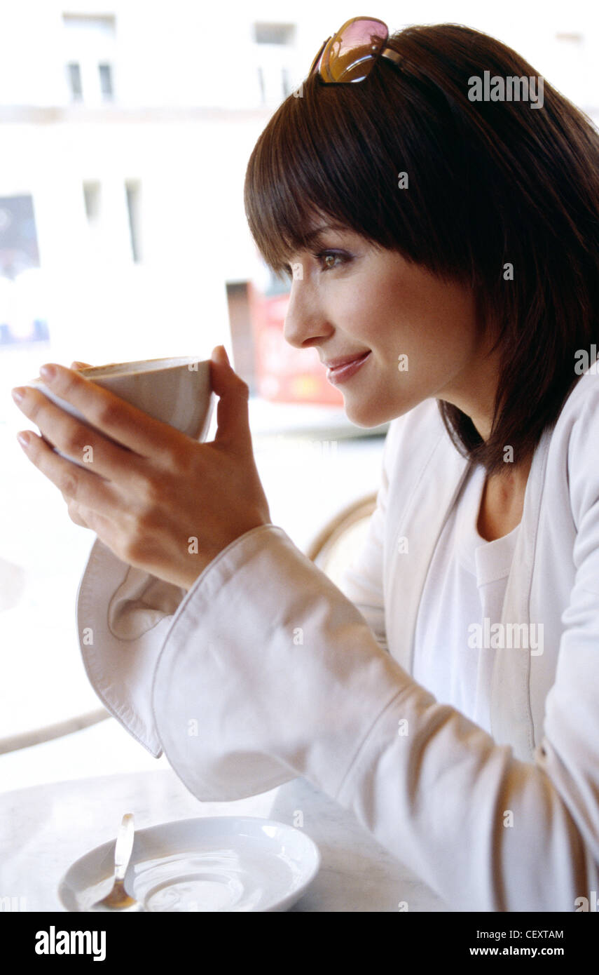 Female shoulder length brunette hair, wearing a white top, sunglasses on top of head and white jacket, sitting in a street Stock Photo