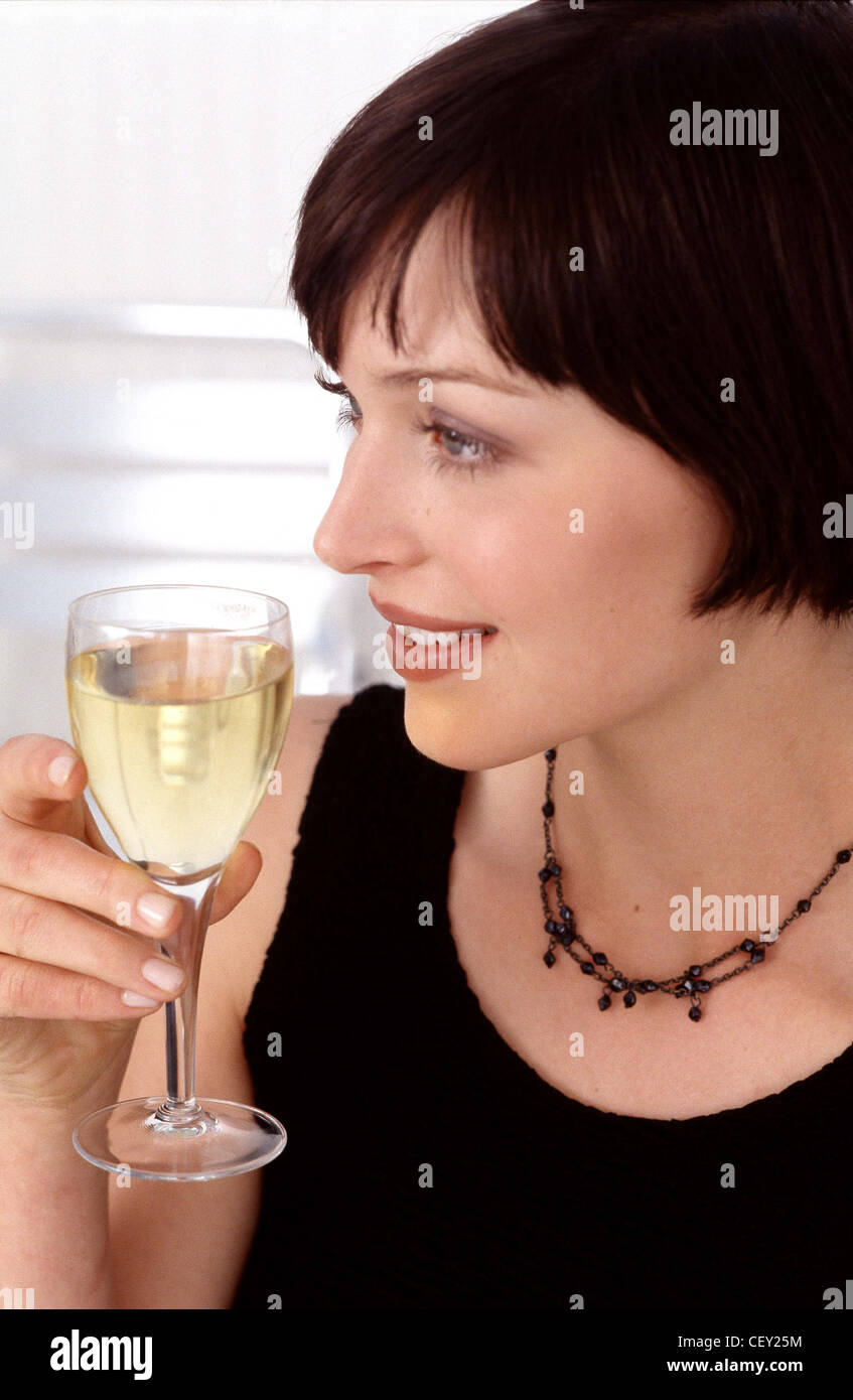 Semi profile of female short brunette hair and fringe wearing black dress and black necklace holding glass of white wine Stock Photo
