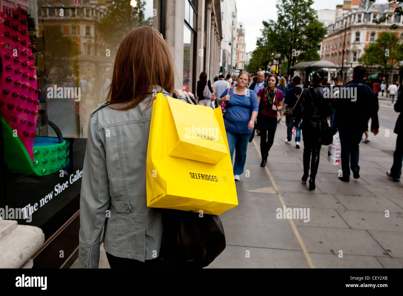 A young lady on Oxford Street with bright yellow shopping bags from Selfridges (Model Released) Stock Photo