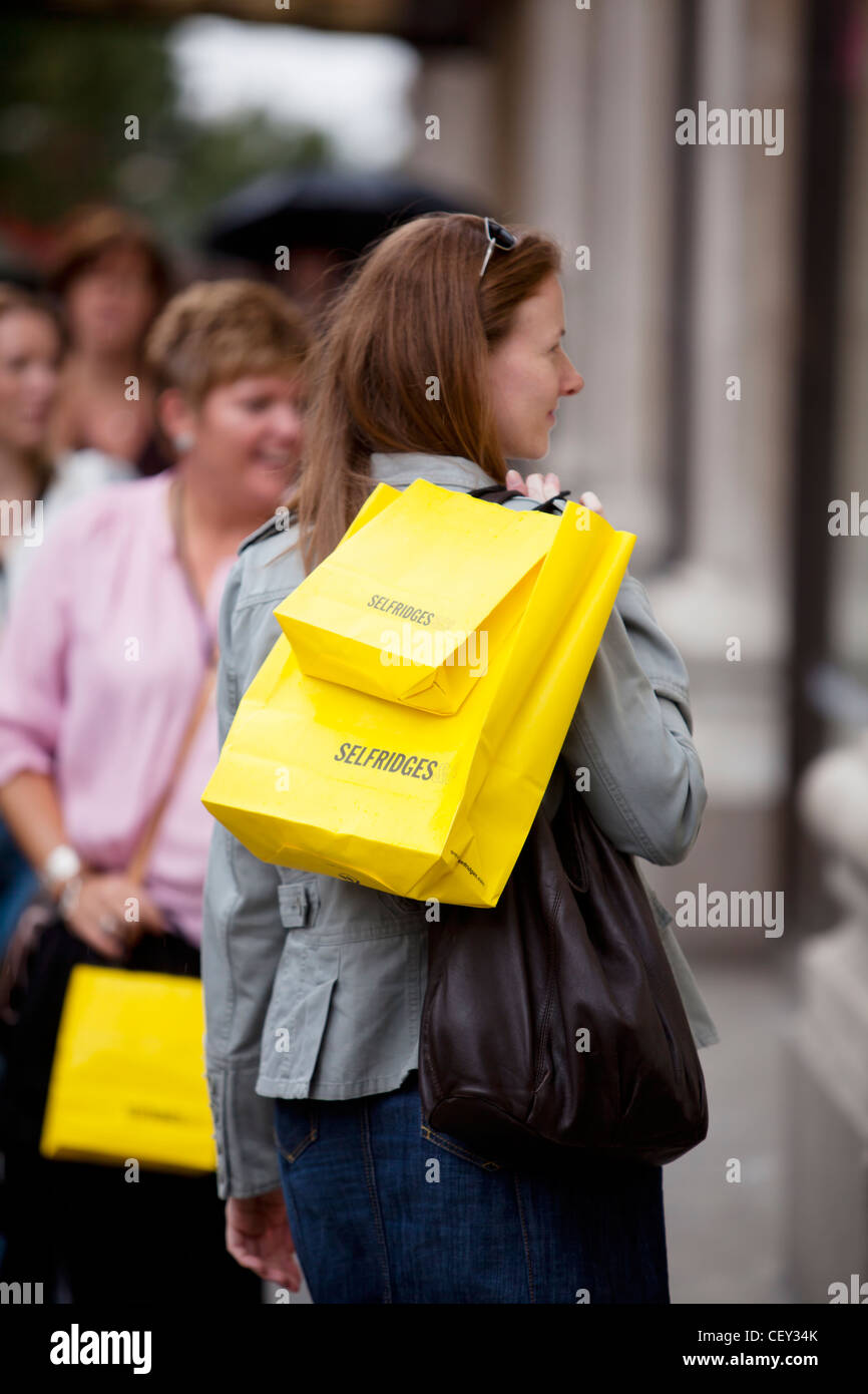A young lady on Oxford Street with bright yellow shopping bags from Selfridges (Model Released) Stock Photo