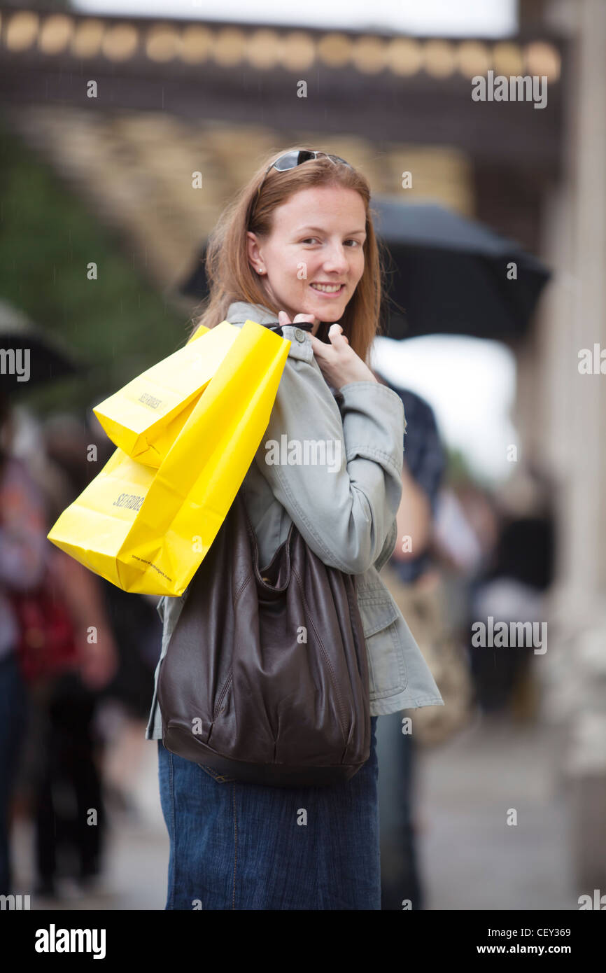 A young lady on Oxford Street with bright yellow shopping bags from Selfridges (Model Released) Stock Photo
