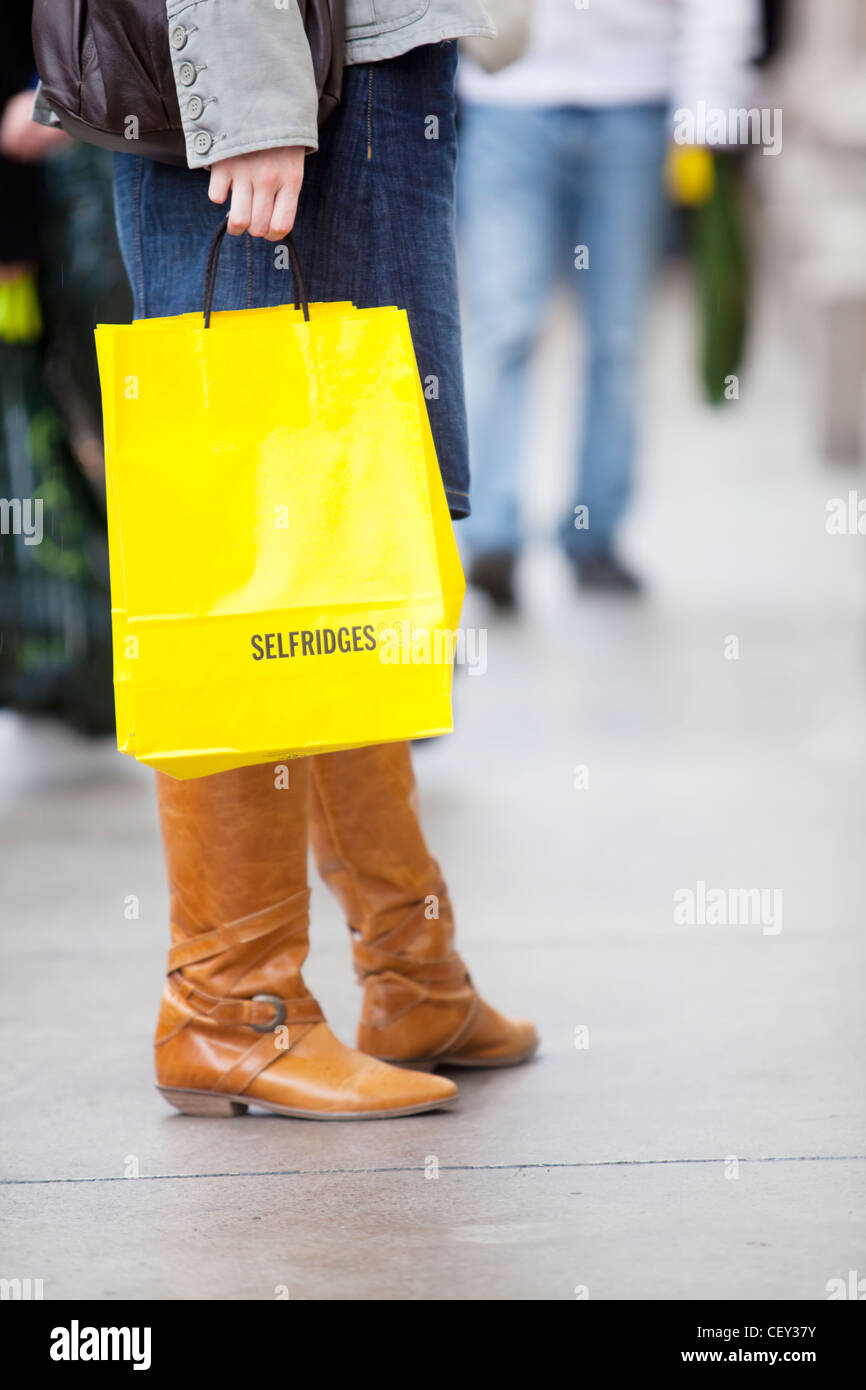 A young lady on Oxford Street with bright yellow shopping bags from Selfridges (Model Released) Stock Photo