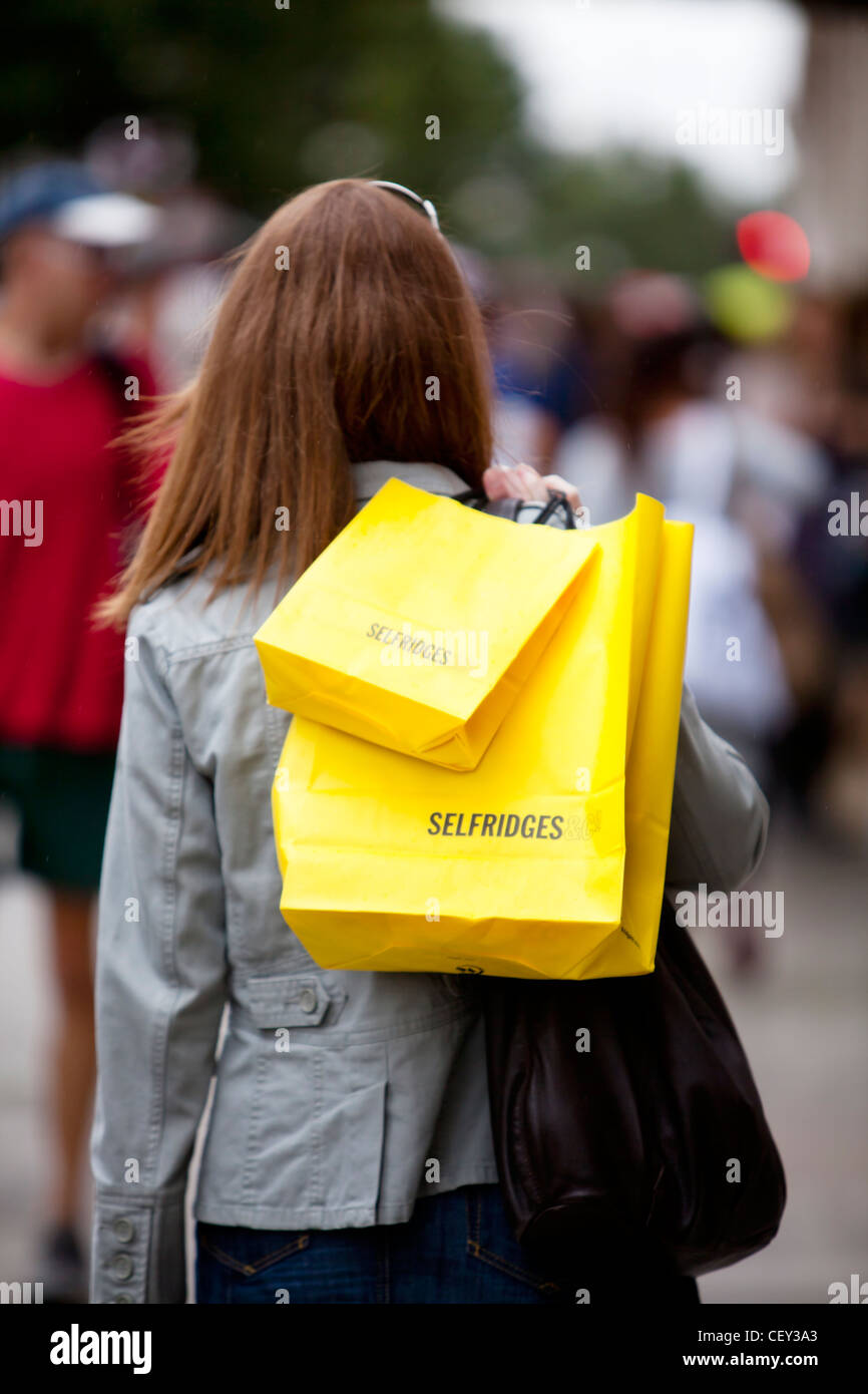 A young lady on Oxford Street with bright yellow shopping bags from Selfridges (Model Released) Stock Photo