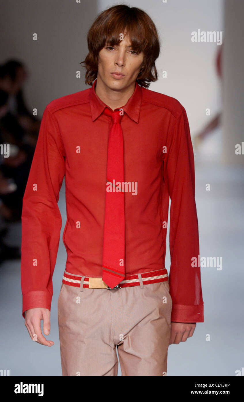 Calvin Klein Menswear Ready to Wear Spring Summer Model long brown hair wearing red shirt, red tie and brown trousers red Stock Photo