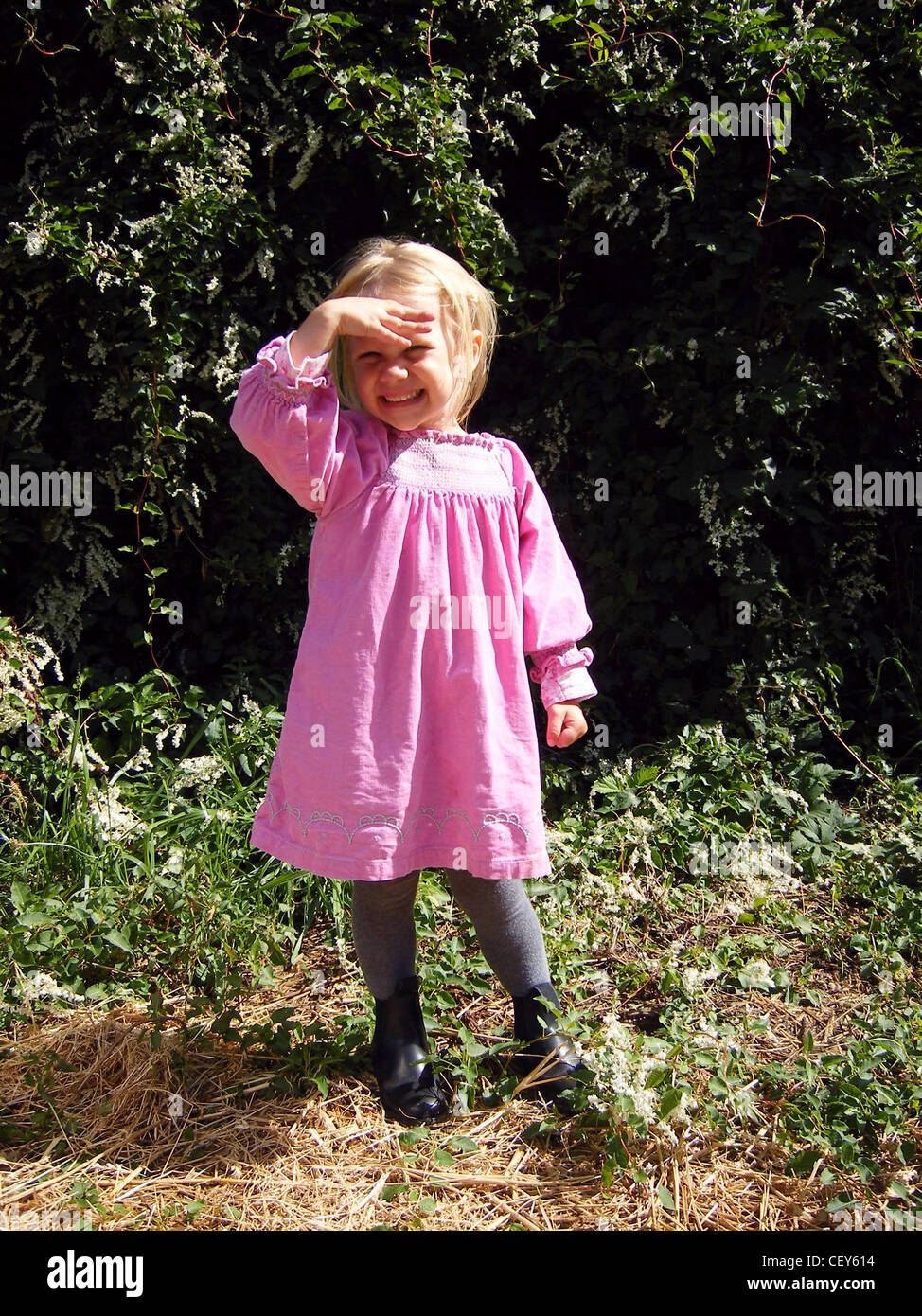 A young blonde female wearing a pink smocked dress grey tights and black  ankle boots, holding her hands up to shield her eyes Stock Photo - Alamy