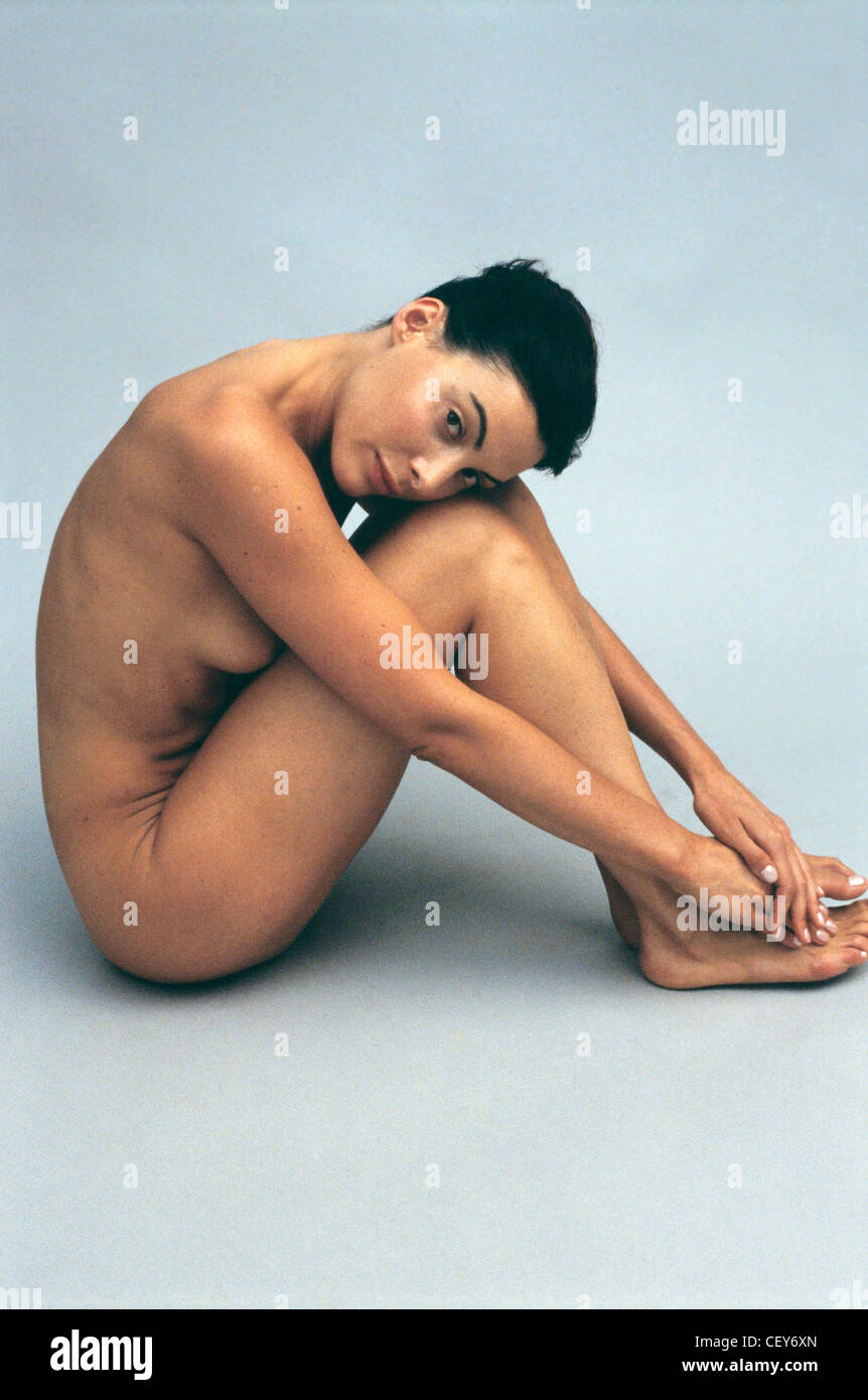 Nude female sitting sideways to camera knees to chest leaning forward hands  on feet head resting on knees head turned towards Stock Photo - Alamy