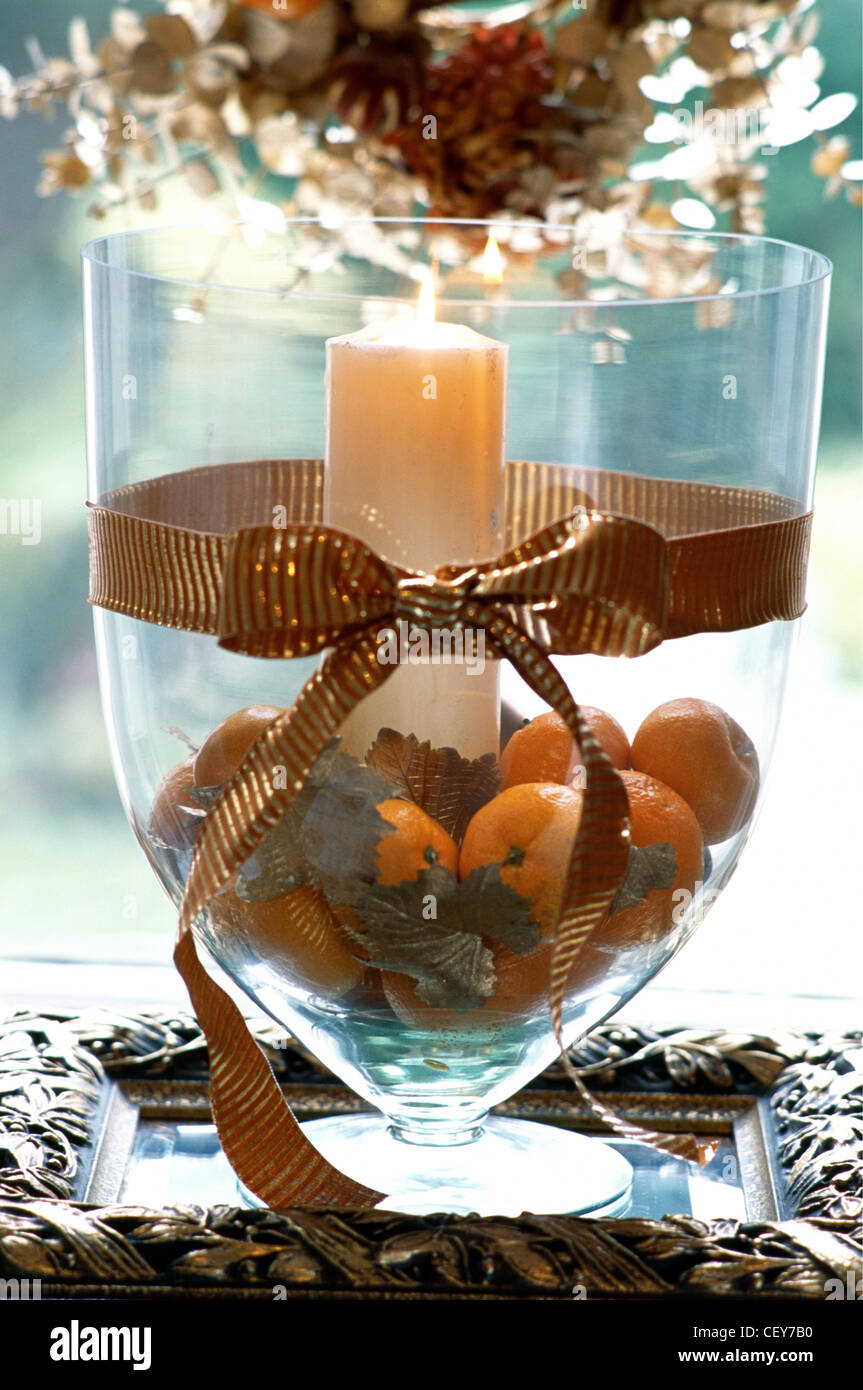 Decorating Gold at Christmas Large glass vase filled oranges, gold leaves  and lit candle Wide gold ribbon tied in a bow around Stock Photo - Alamy