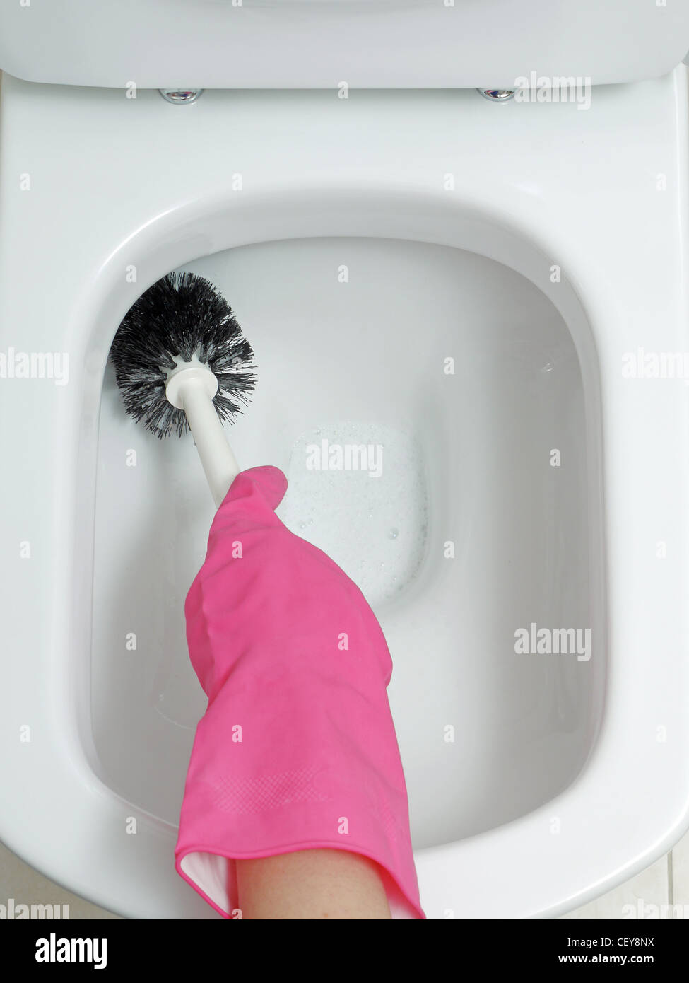 Female hand in pink rubber glove cleaning toilet bowl using brush Stock