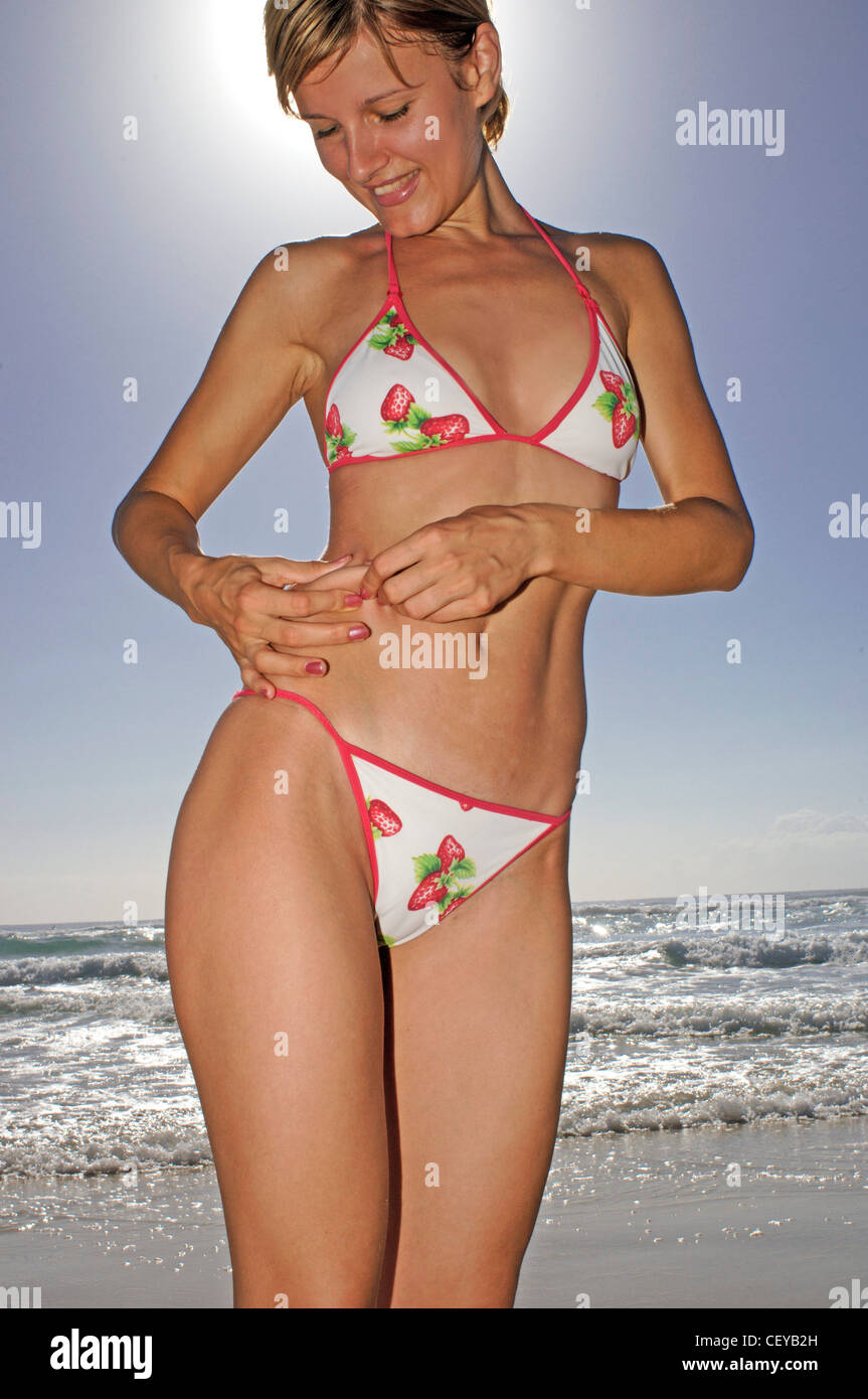 Female, short blonde hair, white bikini with red edging and strawberry  pattern, standing on beach, pinching waist Stock Photo - Alamy