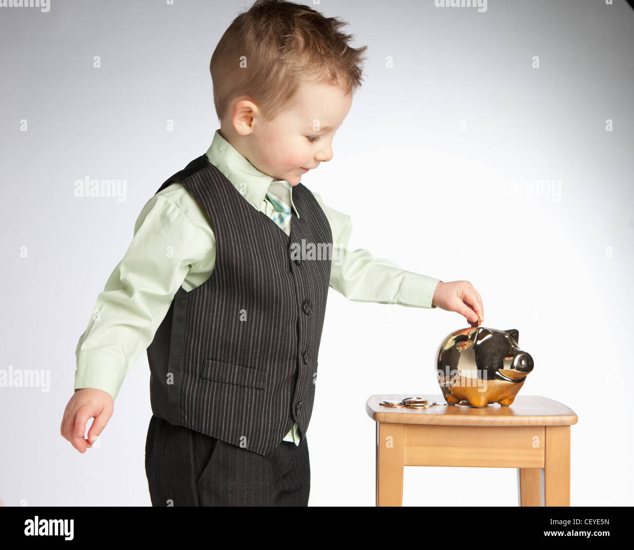 a young boy wearing a vest puts money into a piggy bank; edmonton