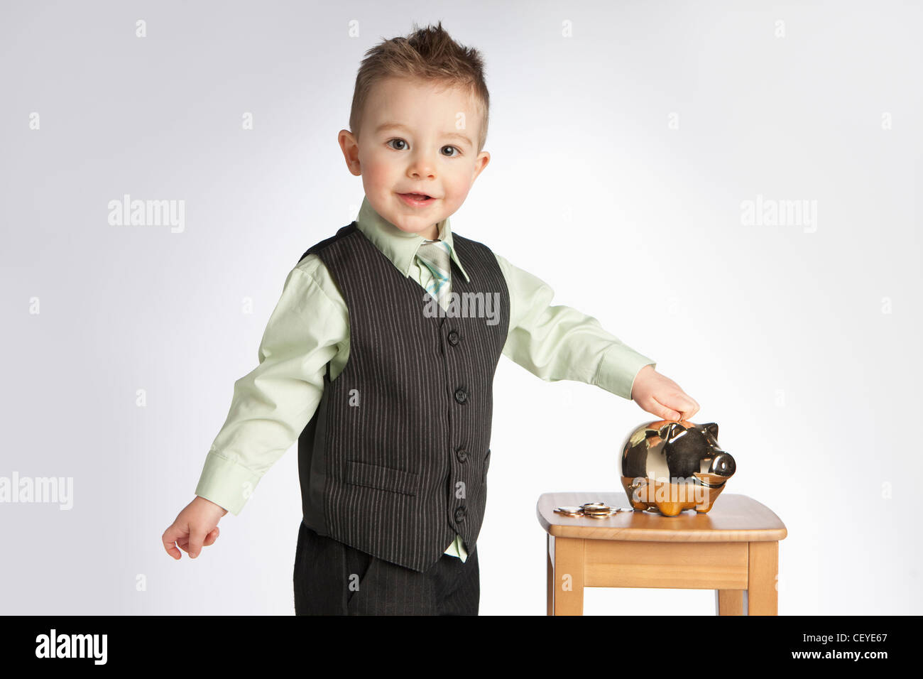 a young boy wearing a vest puts money into a piggy bank; edmonton