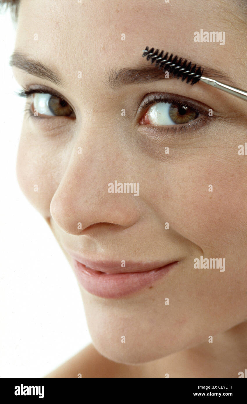 A close up image of female's face, brushing eyebrows, smiling, looking