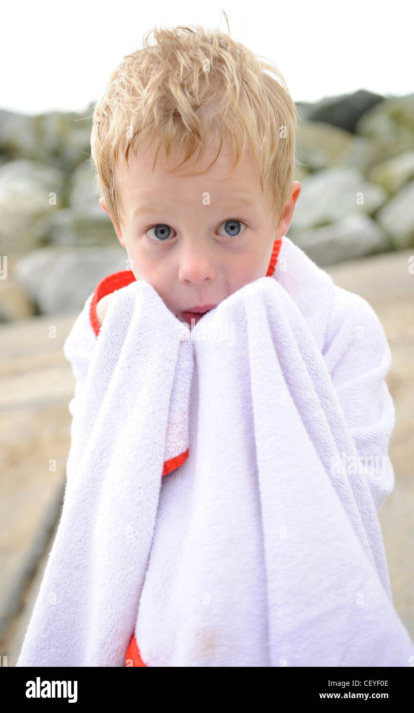 Male Child With Blonde Hair Standing On The Beach Wrapped In
