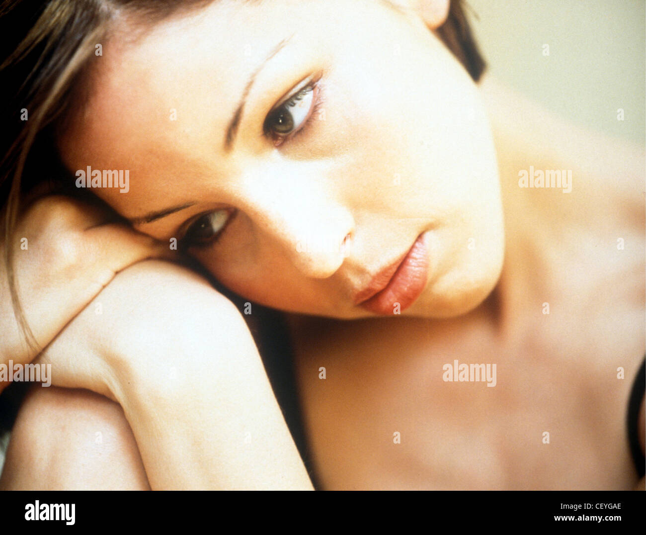 Female with short brunette hair, wearing subtle make up, resting her head on hands, unsmiling, looking down Stock Photo