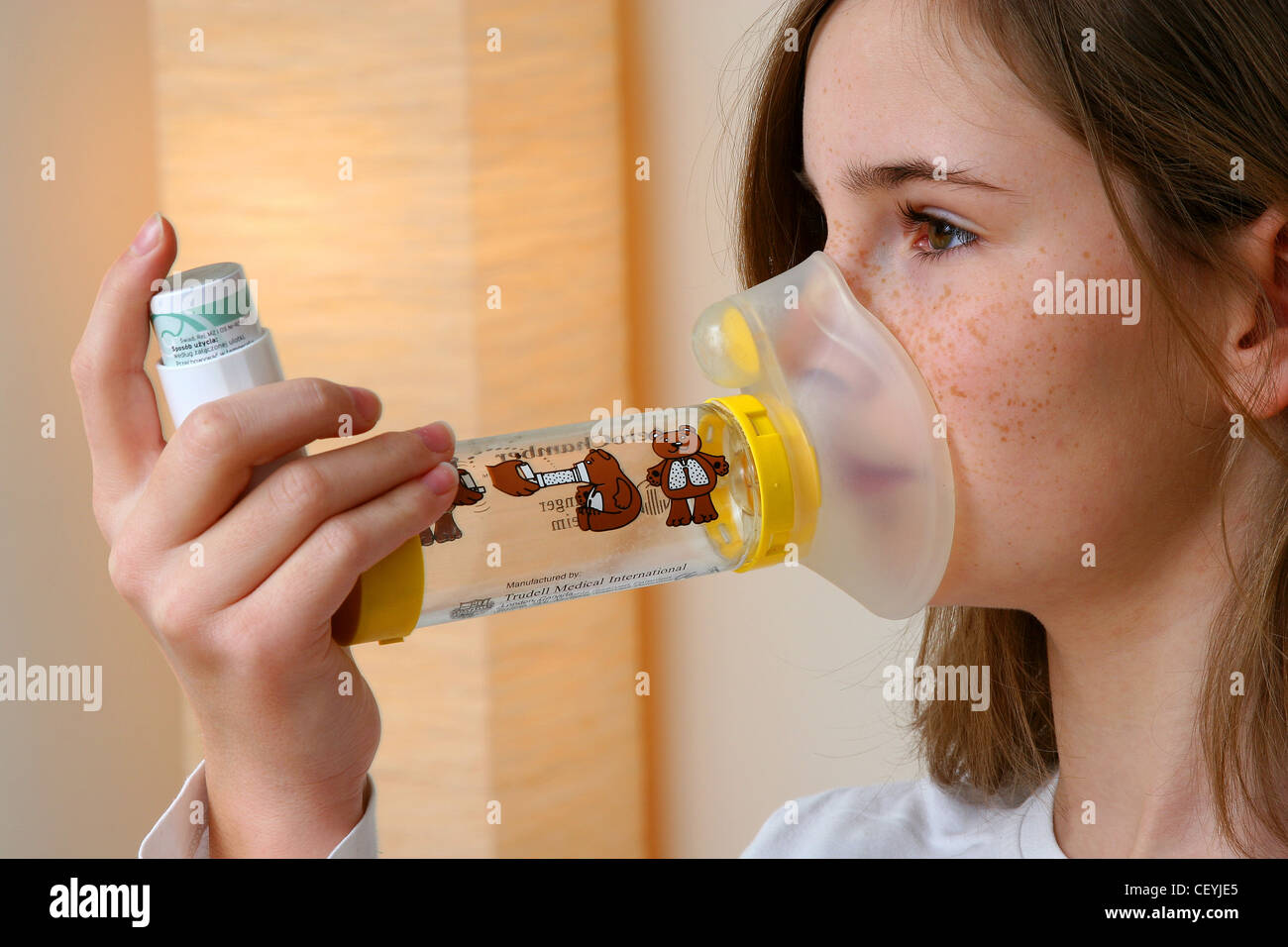 A young female holding an inhaler attachedt to a plastic spacer devise to her face, to treat asthma Stock Photo