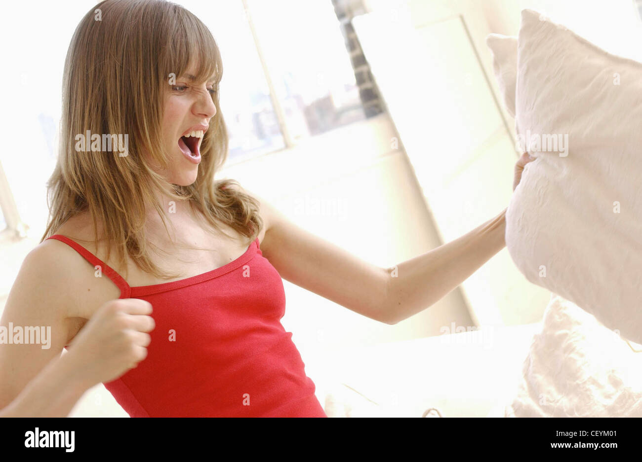 Semi profile of female long light brown hair and fringe wearing subtle make up and red vest top, punching pillow angry Stock Photo