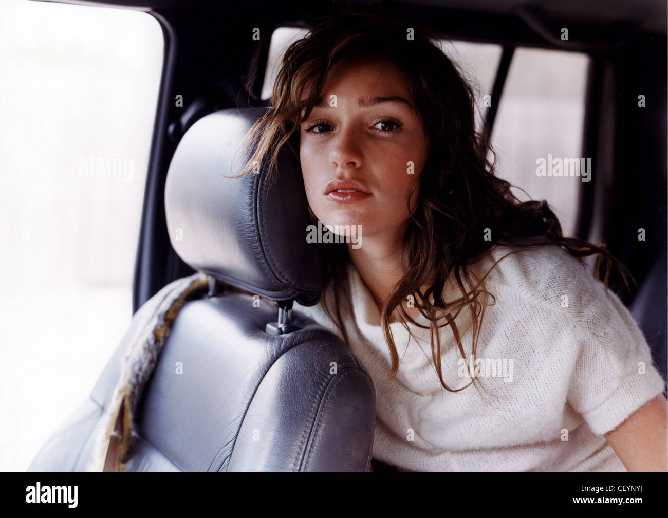 Female long brunette hair wearing cream knitted t shirt sitting in back of car leaning forward over front seat looking to Stock Photo