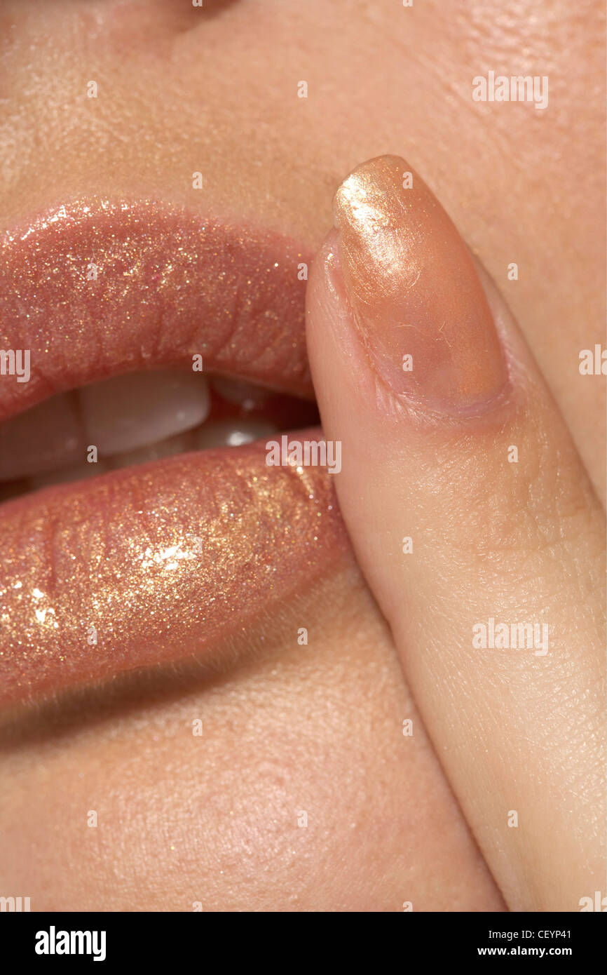 Close up metallic gold lips, finger with matching glittery gold nail polish touching side of lips Mouth slightly open Stock Photo