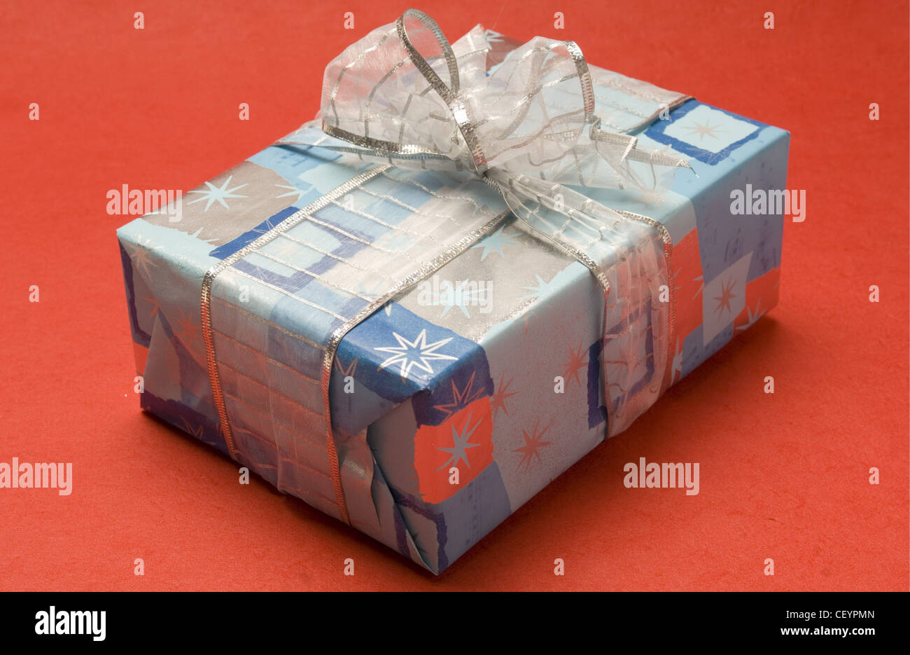 Single wrapped gift: blue and silver star patterned wrapping paper with silver ribbon, pictured on plain pink background Stock Photo