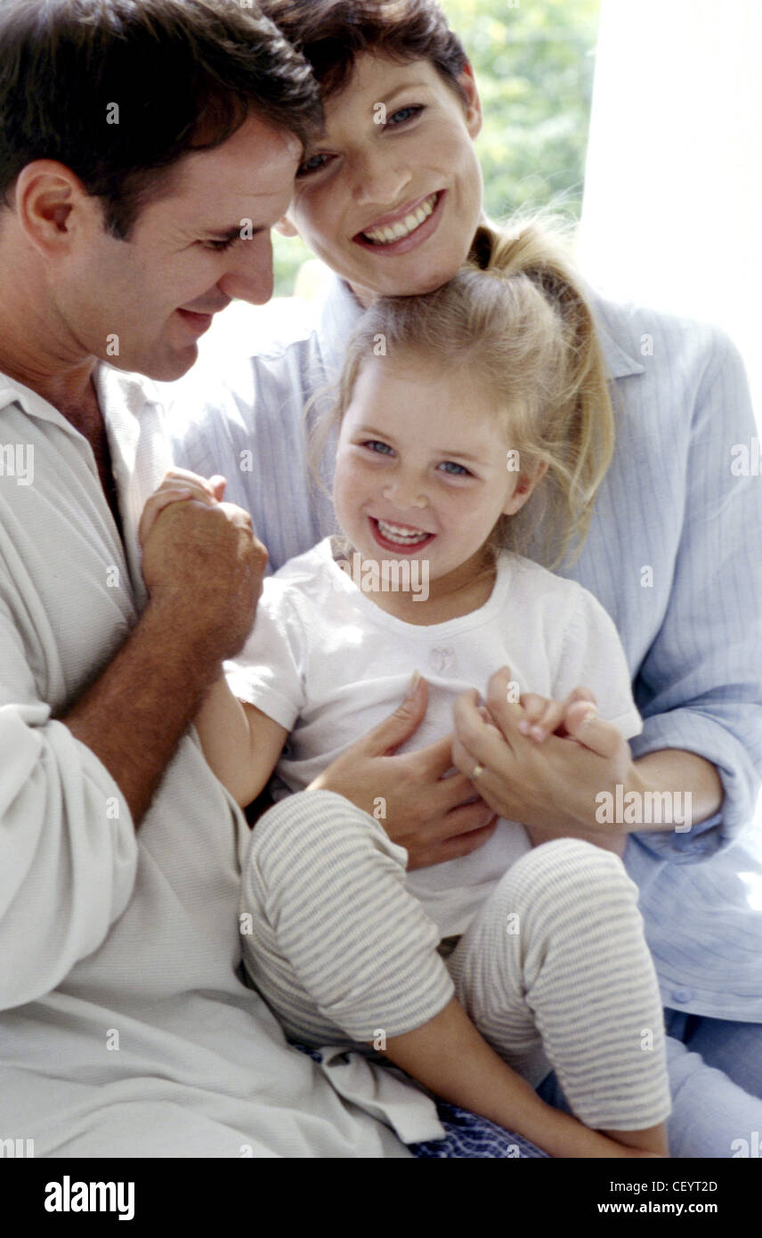 Brunette male and female with blonde female child under sitting on laps ...