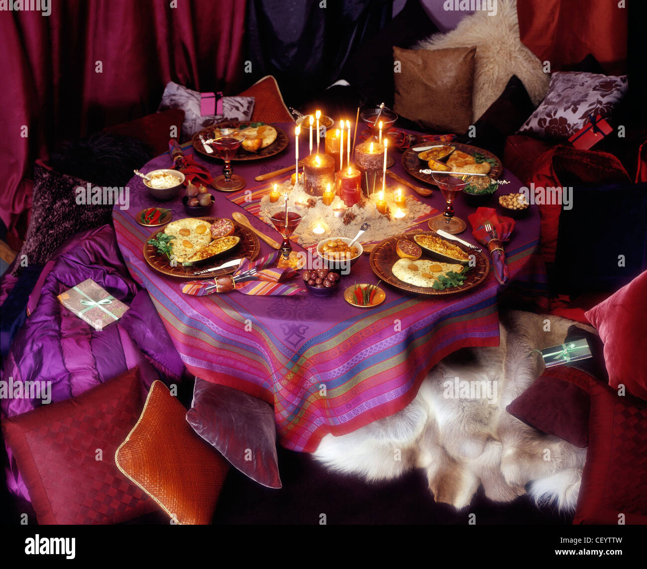 Indian Themed Table Settings Table pink and purple patterned table cloth, centre piece of various lit candles in a mound of Stock Photo