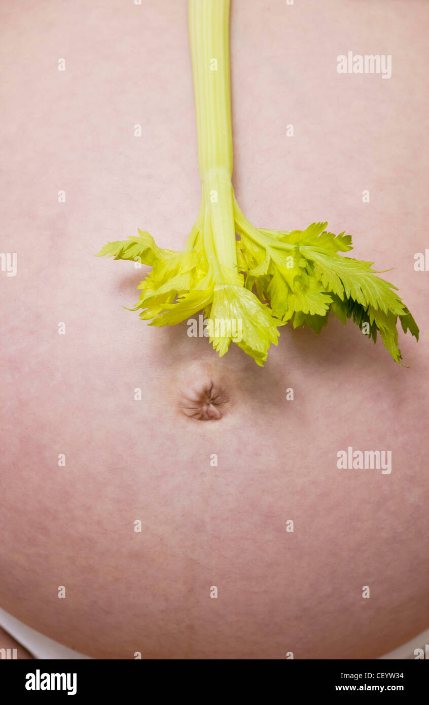 Anonymous cropped shot of a heavily pregnant female holding a celery