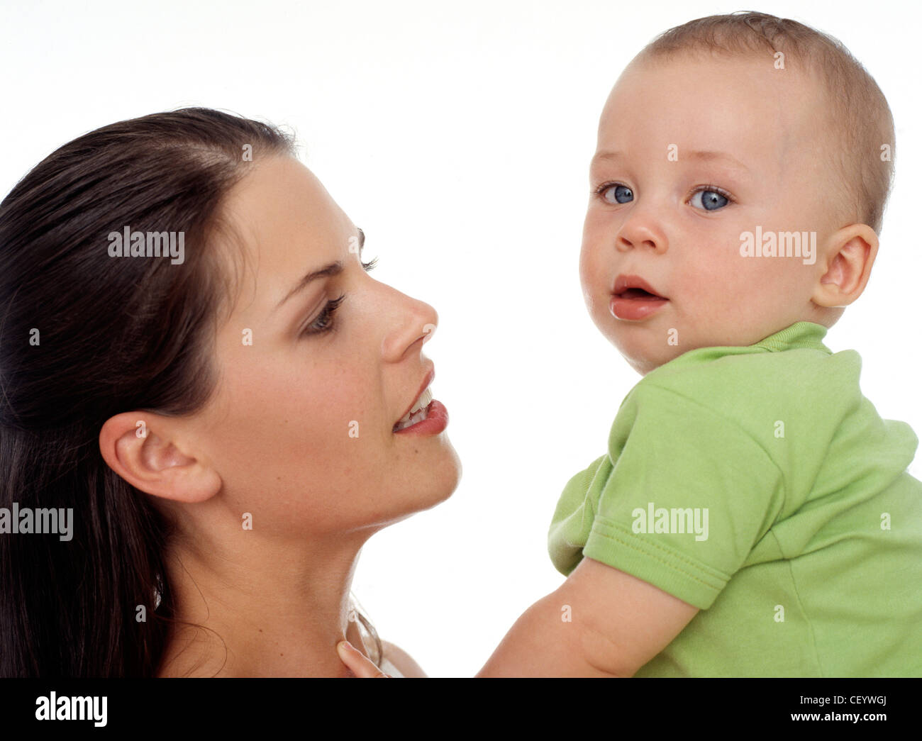 Mother with straight brunette hair holding her baby, to face her and talking to it, baby looking over shoulder to camera Stock Photo