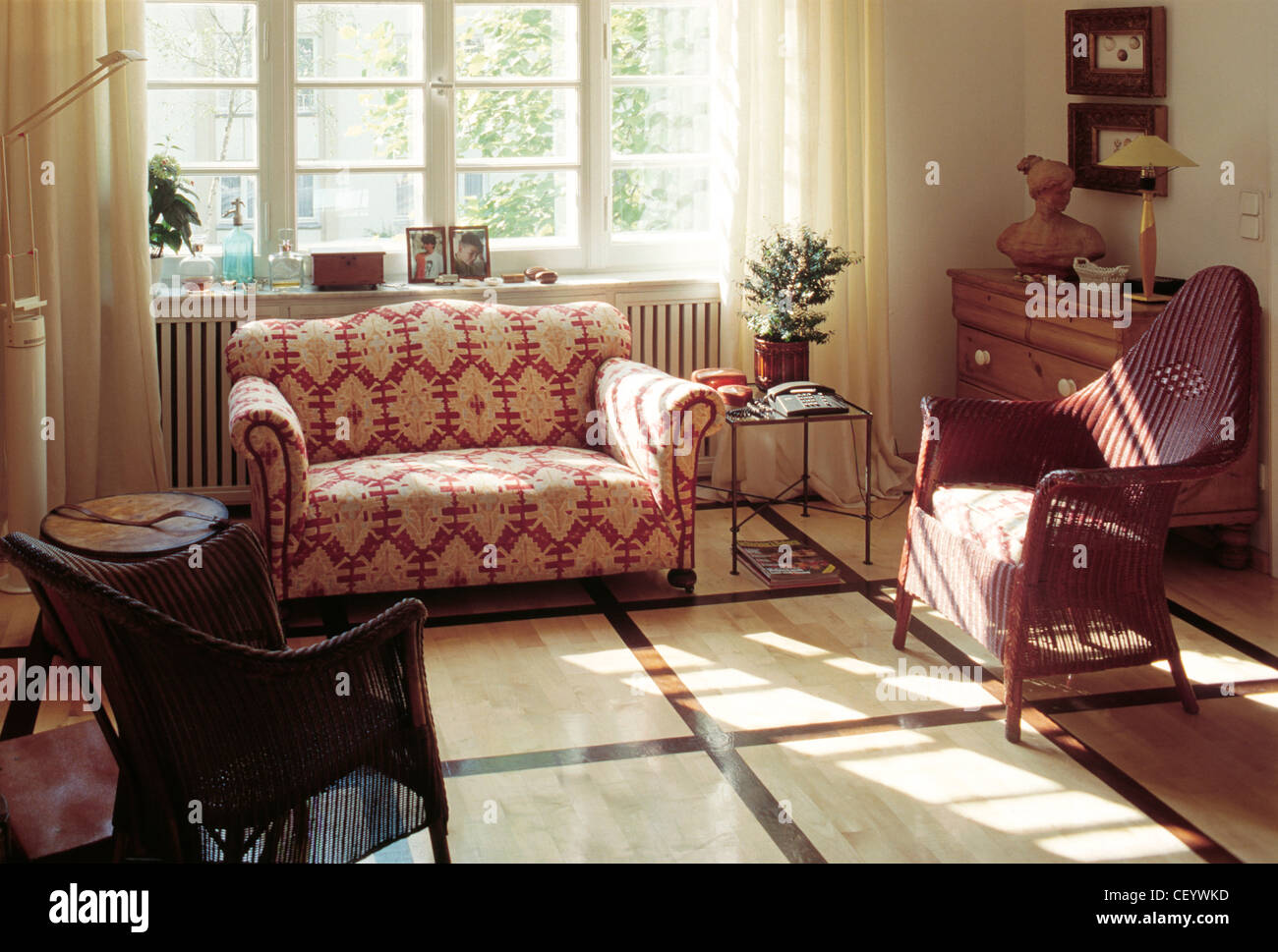 REAL HOMESLiving area two seater patterned armchair, two wicker chairs, window cream curtains, laminate floor, wood chest of Stock Photo