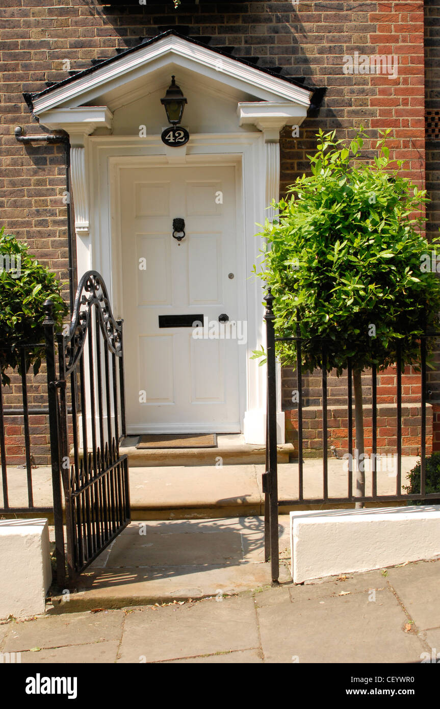 A White Front Dowith Pediment Black Railings And A Gate And