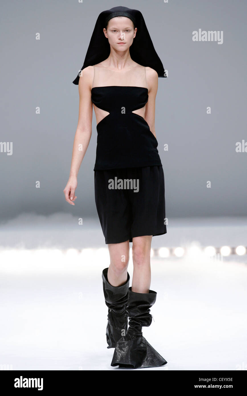 Rick Owens Paris Ready to Wear Spring Summer Model wearing a black knee length dress see through top and cut out detail around Stock Photo