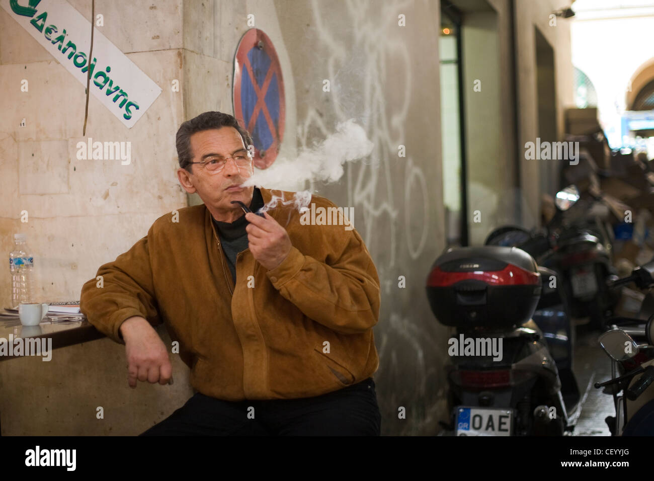 A man lights and smokes a pipe outside a small cafe in the Athens Central Market on Athinas Street. Athens, Greece Stock Photo
