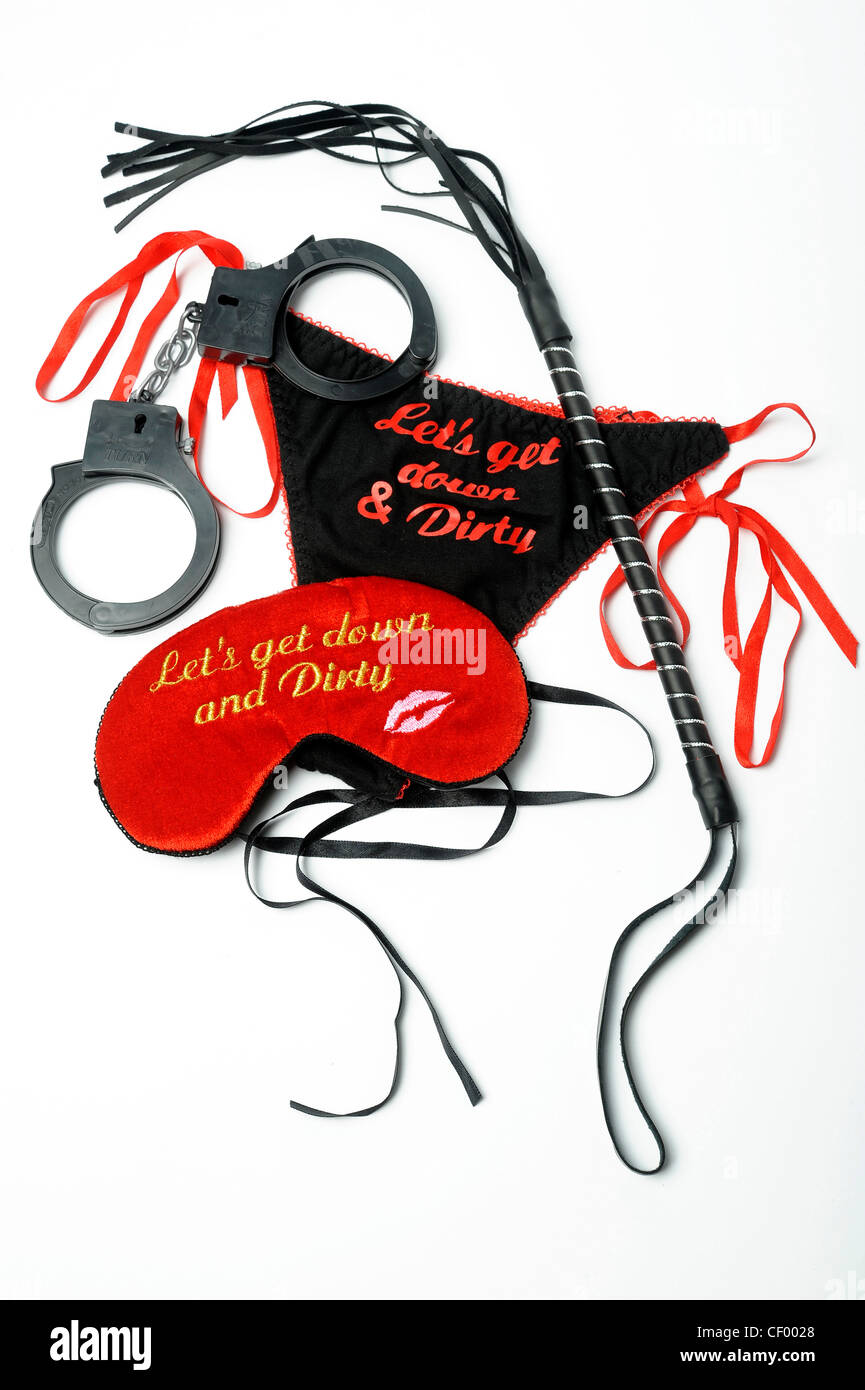 Still life image of a red sleeping mask, black thong reading Lets get down  and dirty, black leather whip and black handcuffs Stock Photo - Alamy