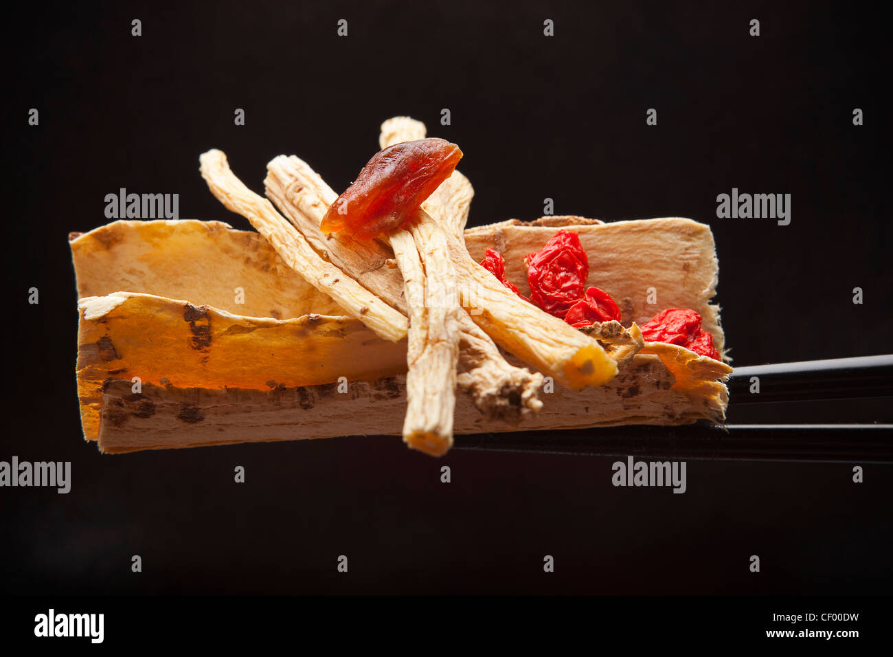 Pak Kee Dong Sum ingredients: Dong Sum root, dried Longan; Astragalus root; red Medeberry on chopsticks Stock Photo