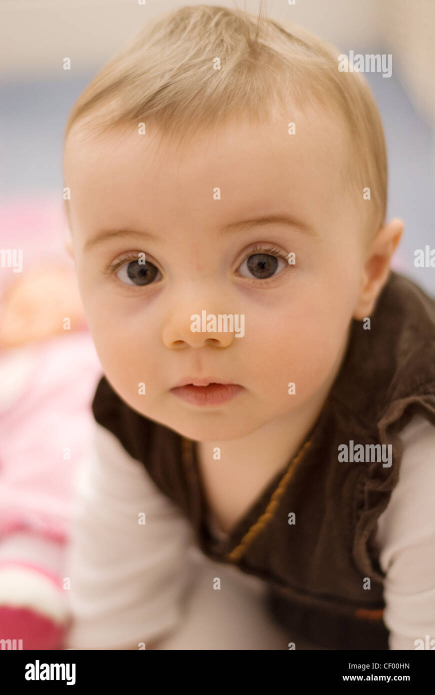 A female baby with fair hair, wearing a white top and brown dress