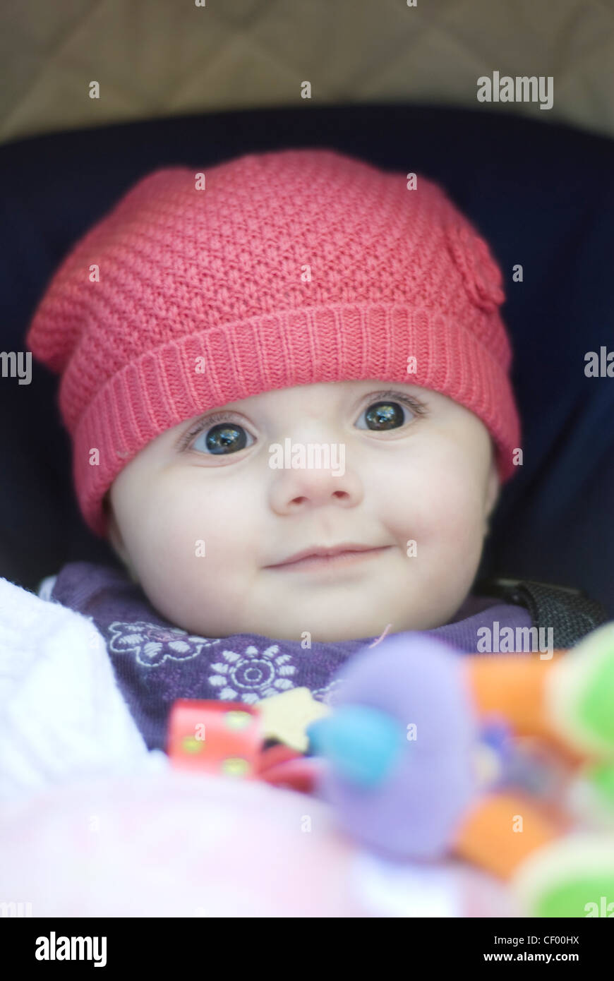 A female baby, wearing a purple dress and red hat, sitting in pushchair
