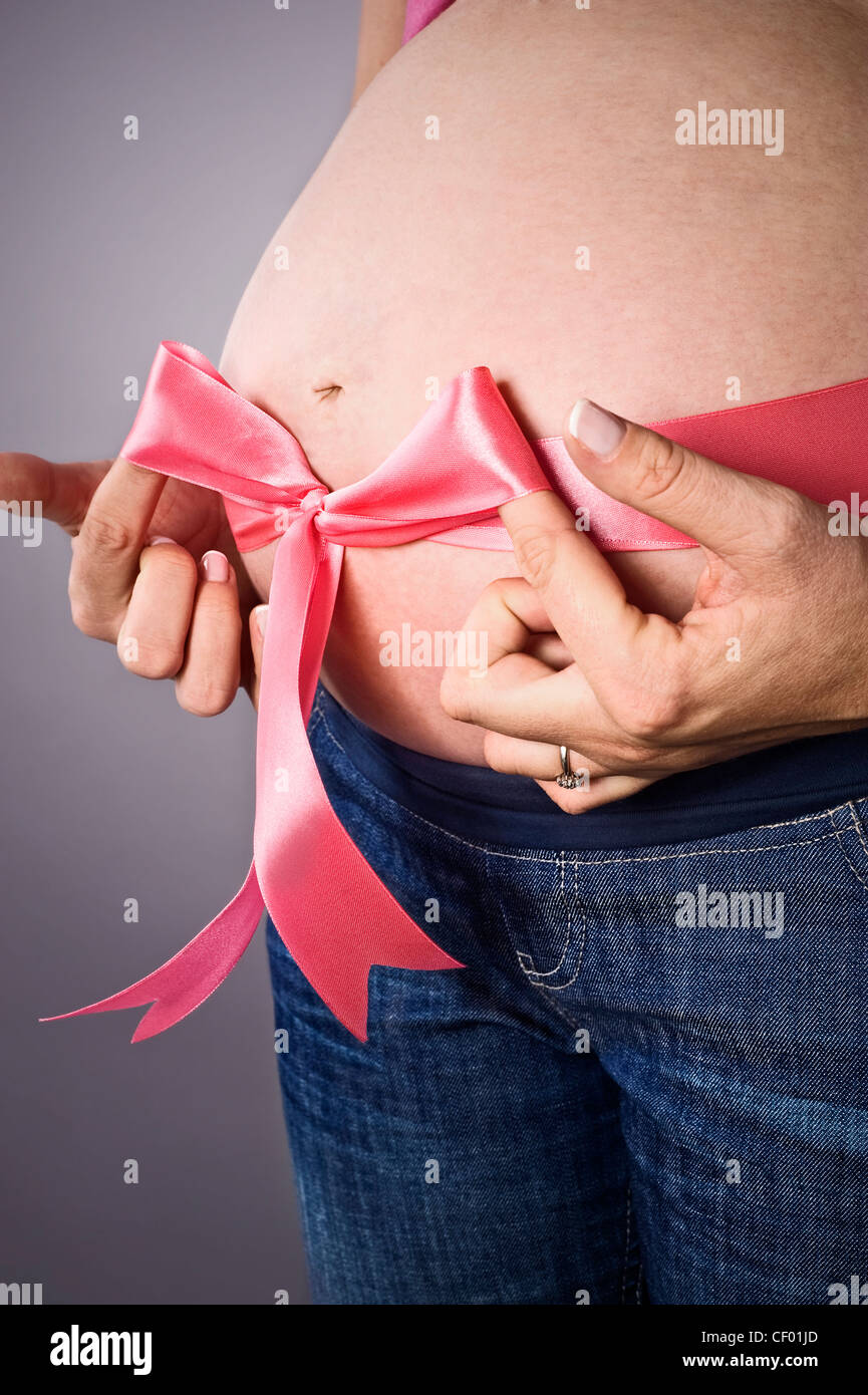 pregnant female tying pink ribbon bow on belly Stock Photo