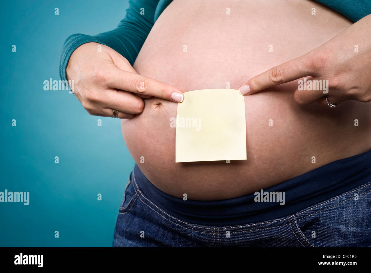 pregnant female pointing at notepaper on her belly Stock Photo