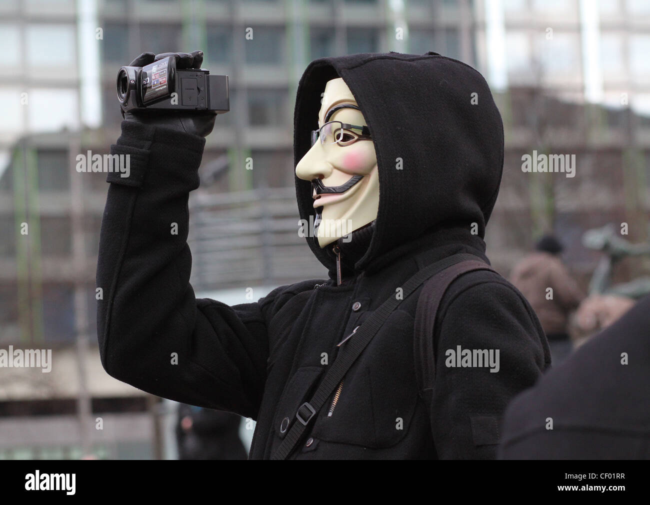 An Anonymous member with a Guy Fawkes mask is recording a protest with a small video cam. Stock Photo