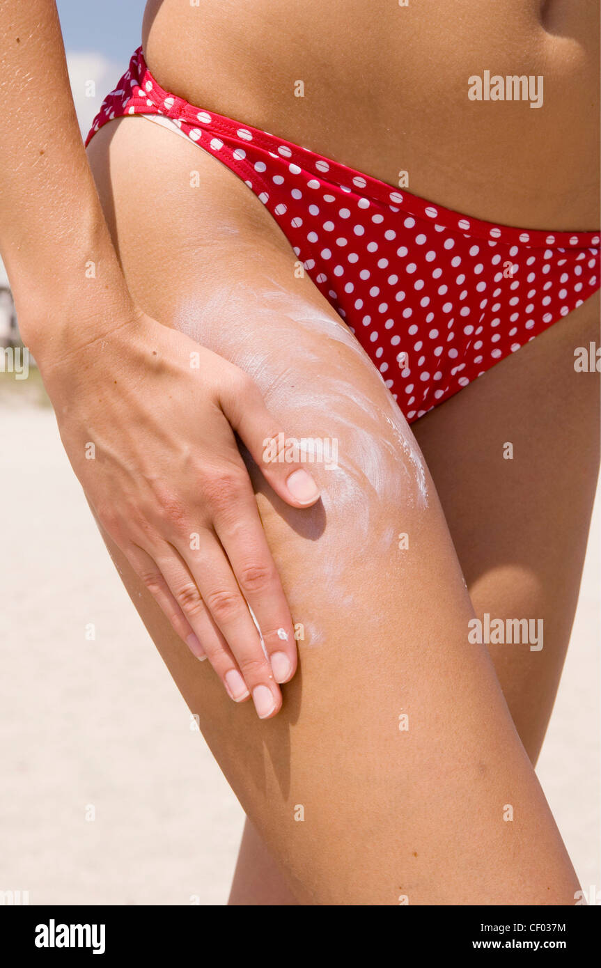 Cropped close up of female wearing red and white polkagot bikini rubbing sun  tan lotion into thigh Stock Photo - Alamy