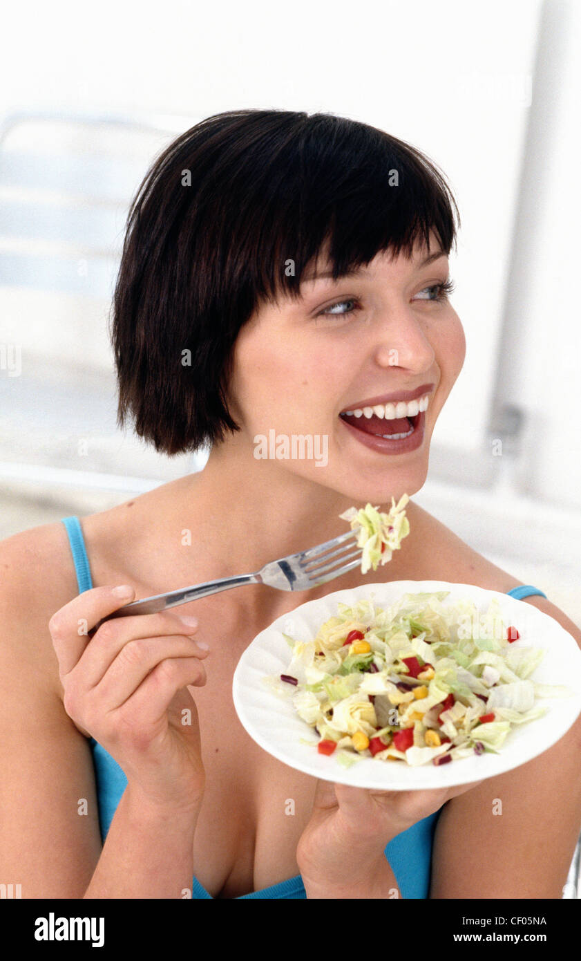 A  Female smiling looking to the right eating a bowl of salad Stock Photo