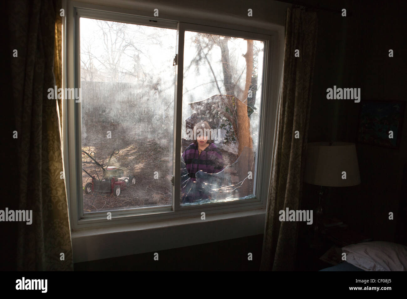 A nine year old boy stares at a broken window. Stock Photo